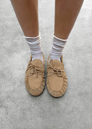 Beige suede leather loafers with moccasin stitching and lace up detail on a clean background